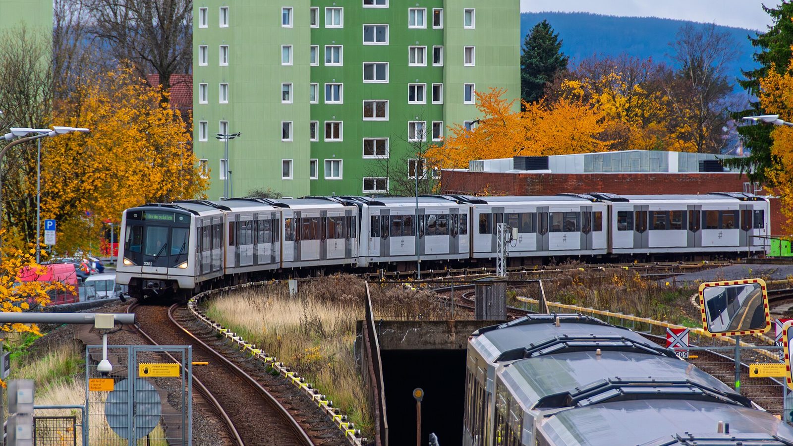 Pociąg metra Ruter typu MX3000 jedzie po torach wśród jesiennych drzew i bloków w Oslo