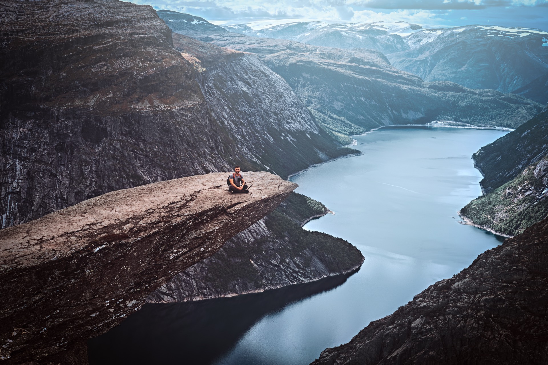 Turysta siedzący na Trolltundze z widokiem na norweski fiord