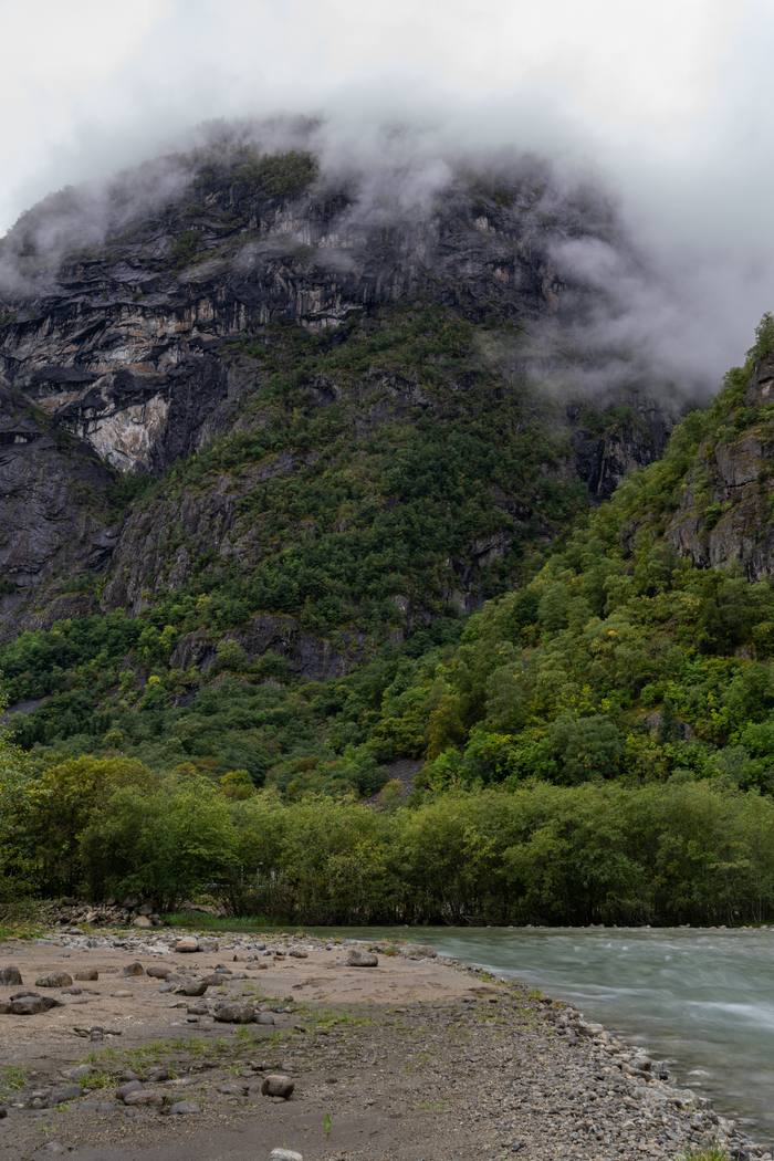 Rzeka o lodowcowej wodzie płynąca u stóp góry spowitej chmurami w Øvre Eidfjord