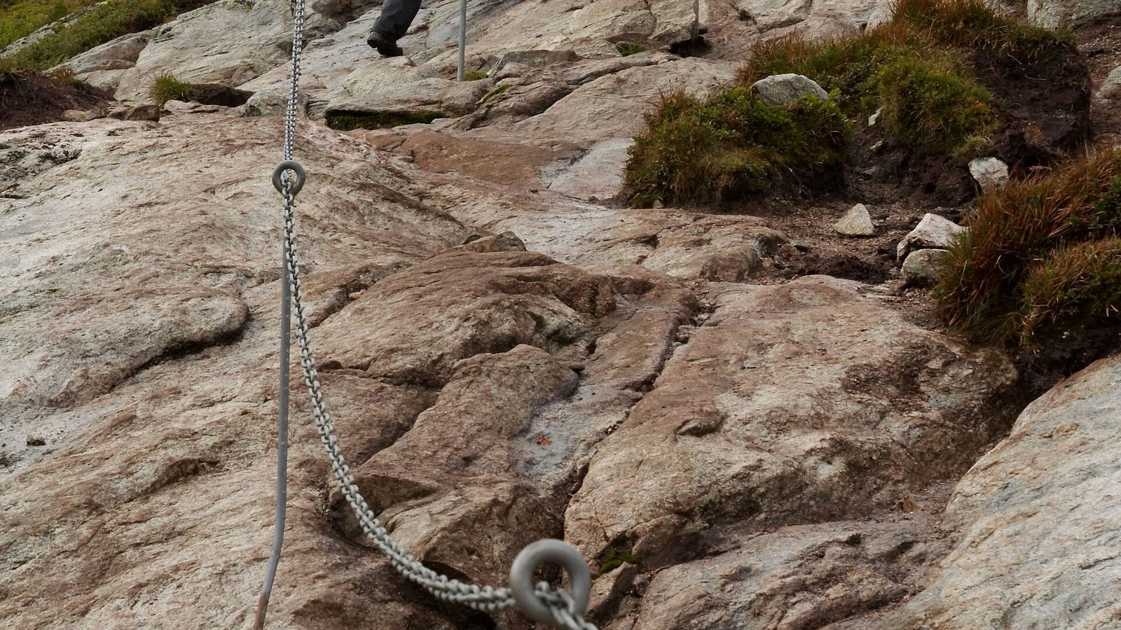 Turysta wchodzący stromą skałą z pomocą łańcucha na szlaku na Kjerag