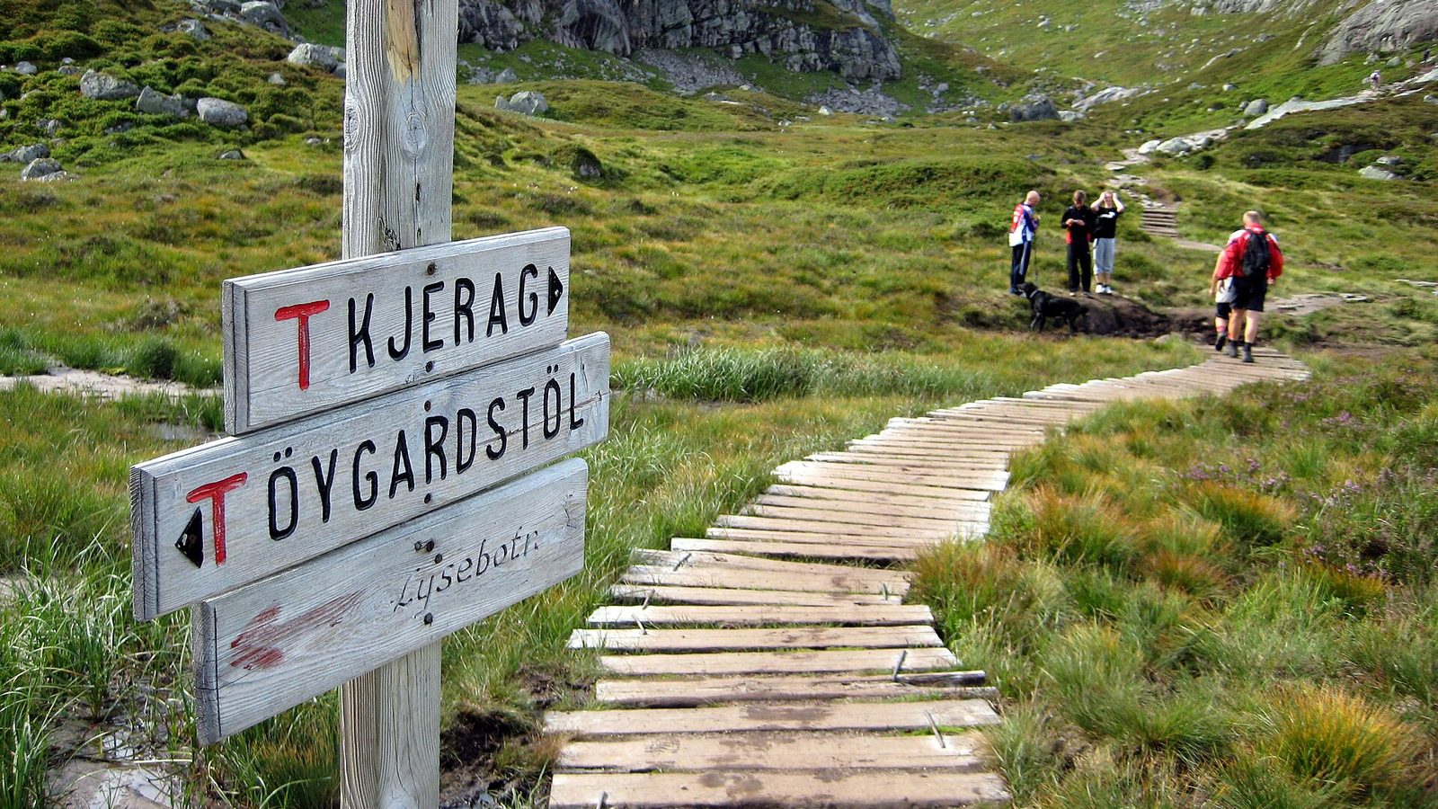 Drogowskaz Kjerag i Øygardstøl z czerwonym T na szlaku z drewnianą kładką