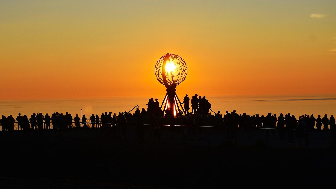 Globus na Nordkapp na tle zachodzącego słońca i sylwetki turystów