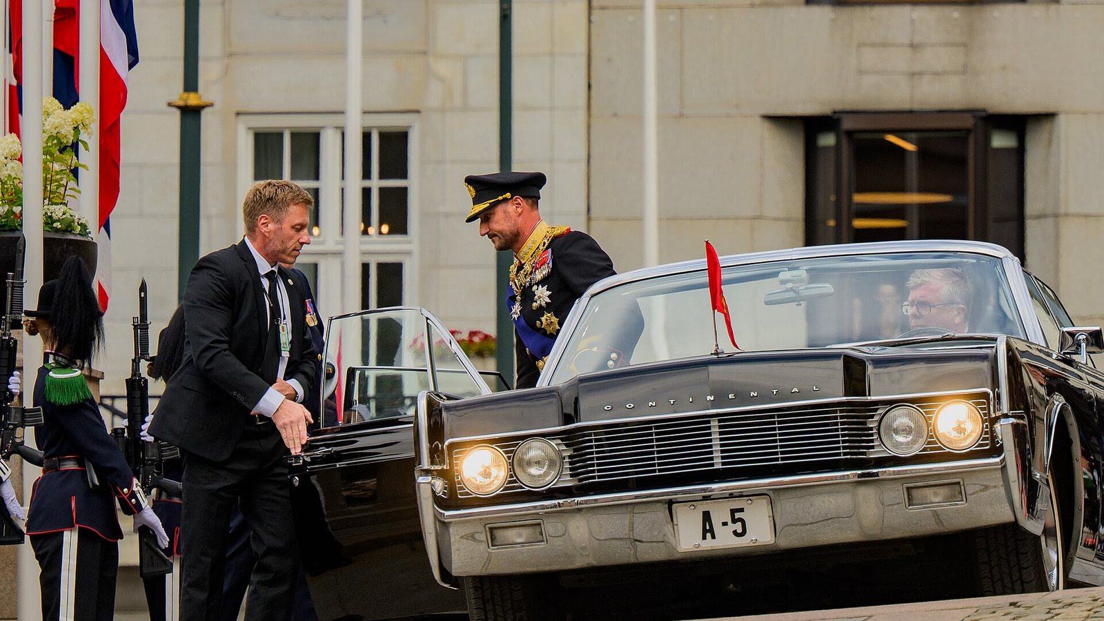 Król Haakon VIII w mundurze galowym wsiada do samochodu przed budynkiem Stortingu w Oslo