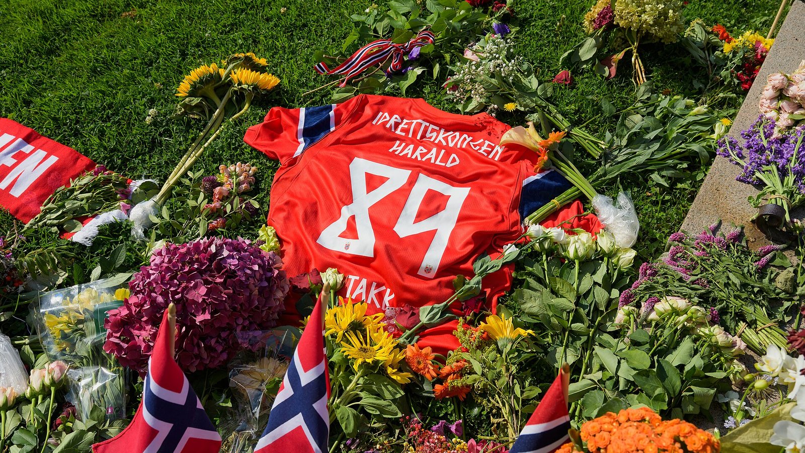 Kwiaty, norweskie flagi i czerwona koszulka z napisem Idrettskongen Harald 89 złożone w hołdzie królowi