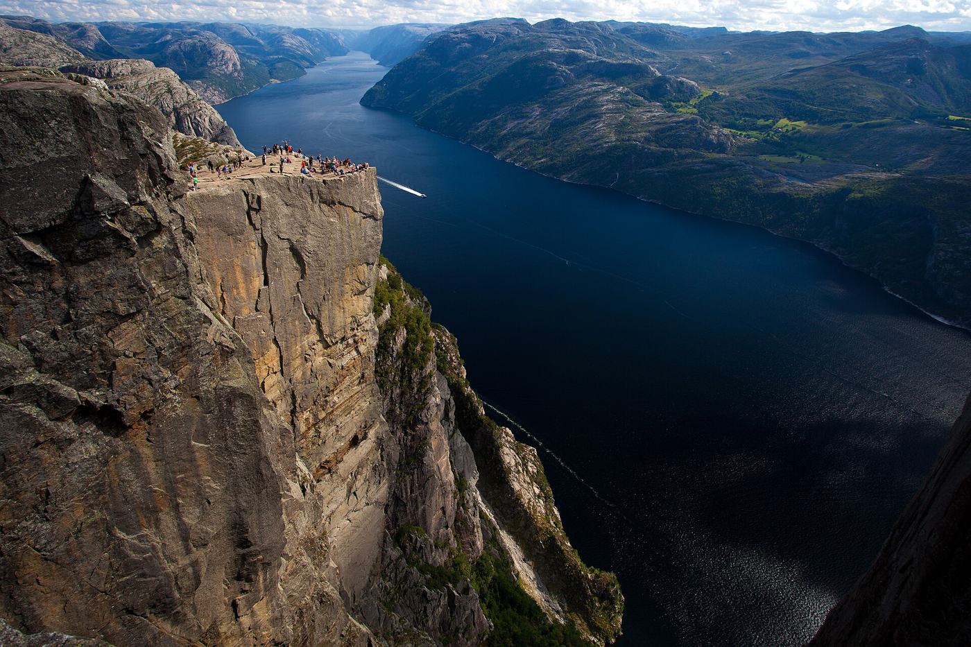 Skalna ściana Preikestolen z turystami na szczycie nad ciemnym Lysefjordem