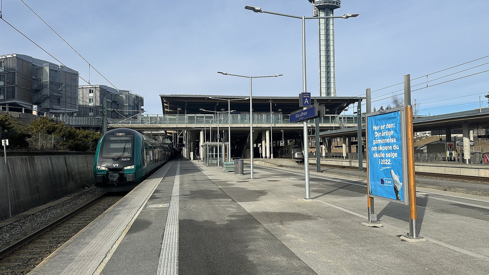 Pusty peron stacji kolejowej Oslo Lufthavn Gardermoen z pociągiem Vy i wieżą kontroli lotów w tle